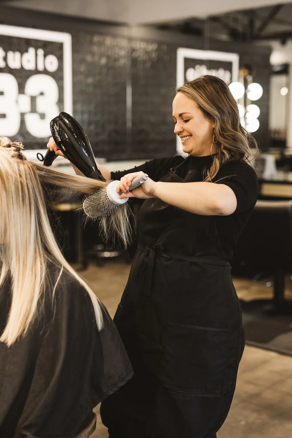A Studio B-3 stylist blow-drying a client beneath the painted Studio B-3 wall